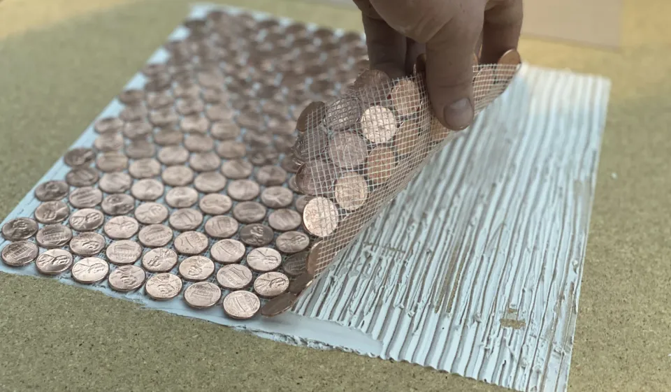 A hand lowering a flexible penny tile into prepared adhesive