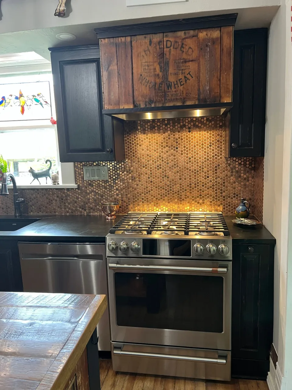 Dark cabinetry and a wood range hood framing a warm penny backsplash