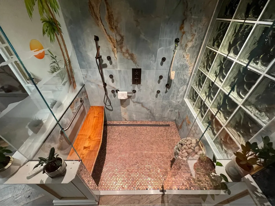 A bathroom with a wood bench, plants, patterned walls, and a penny floor